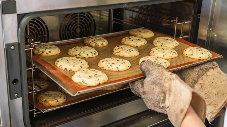 Pale chocolate chip cookies coming out of an oven on a Silpat and baking sheet