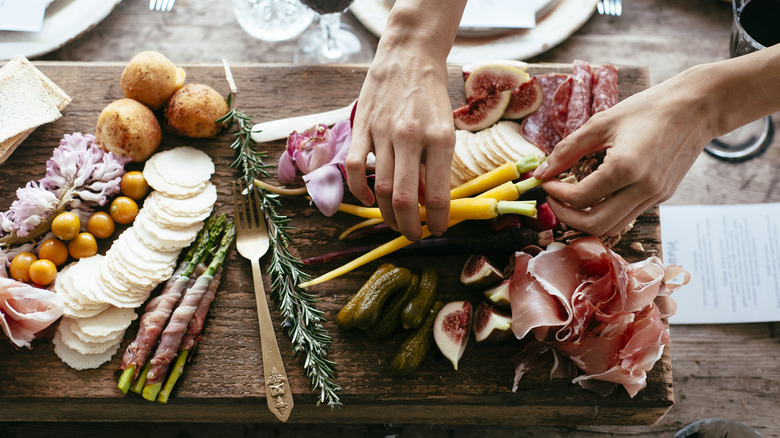 A woman picks up a carrot from a charcuterie board