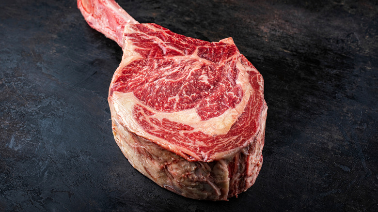 Very well-marbled tomahawk prime steak on stone surface.