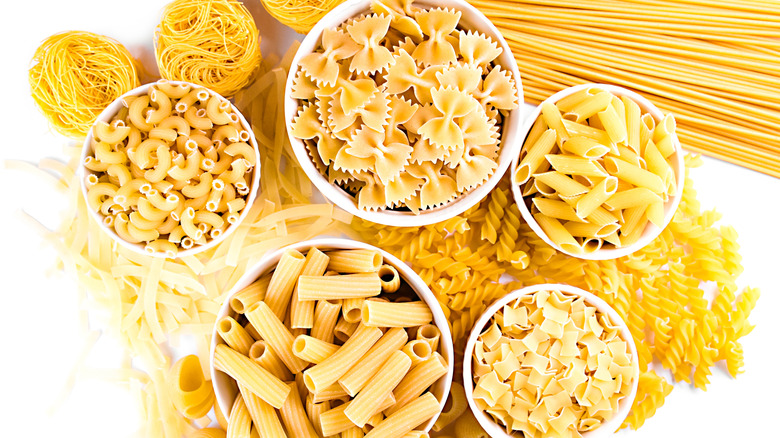 A top-down view of several bowls of different kinds of pasta on a white surface.