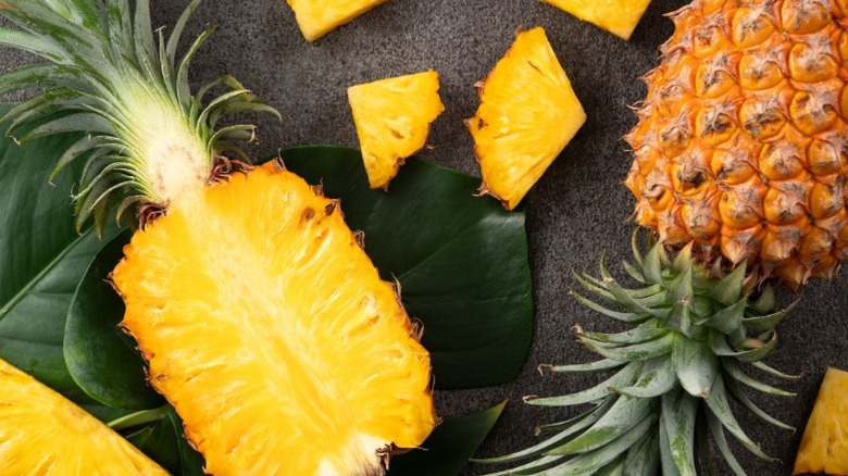 A fresh cut pineapple half and wedges on a black background.