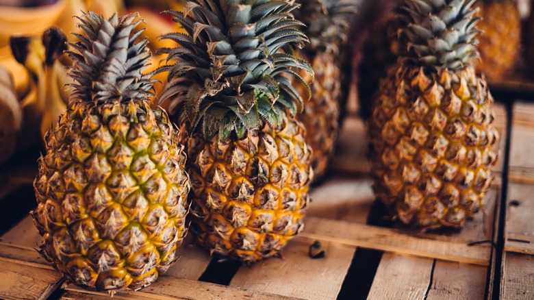 Three pineapples sitting on a wooden crate.