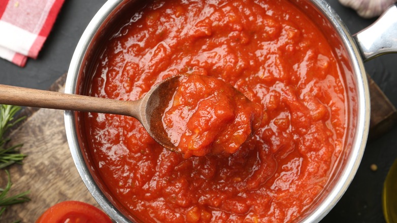 A wooden spoon lifts tomato sauce from a pot