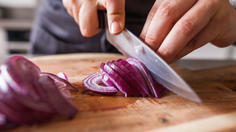 A person cutting red onions on a wooden cutting board.