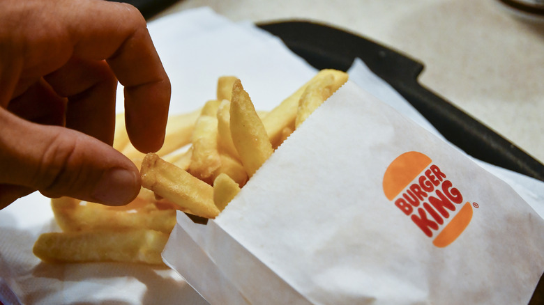 A hand grabbing some french fries from a Burger King-labelled paper bag.