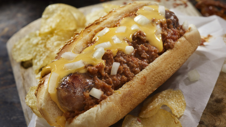 A chili cheese dog with onions and potato chips sitting on a counter