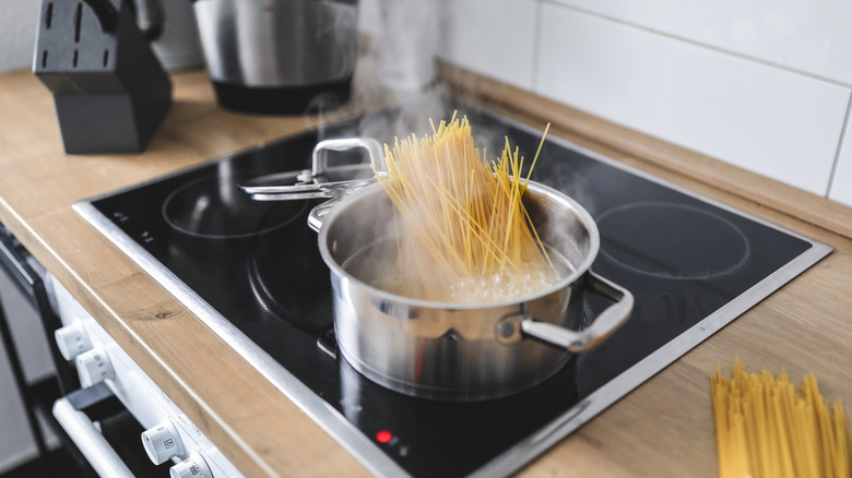 A bundle of uncooked spaghetti sticking out of a pot of boiling water on a stovetop.