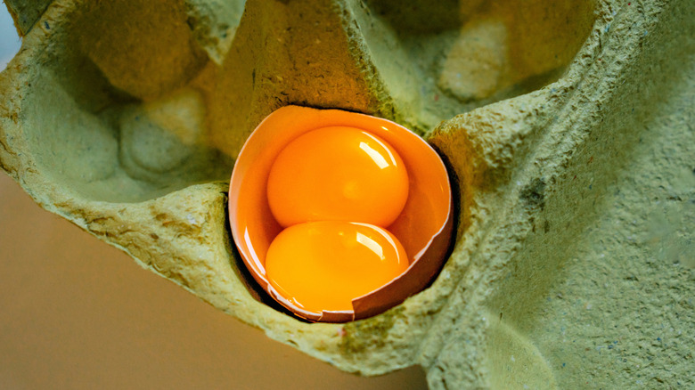 Two egg yolks inside a single egg shell in a cardboard crate