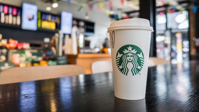 A cup of Starbucks coffee on a wooden table in front of a blurred background.