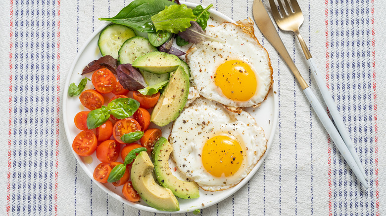 Plate with sunny side up eggs, tomatoes, avocados, and cucumbers