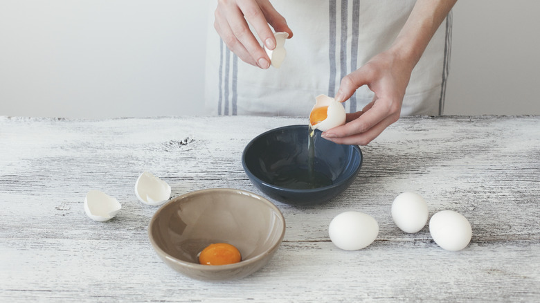hands separating egg whites from egg yolks into two different bowls