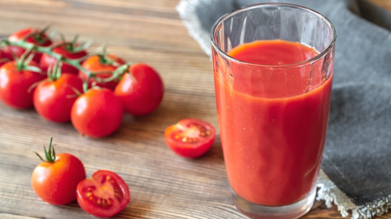 A glass of tomato juice with fresh tomatoes on a wooden table