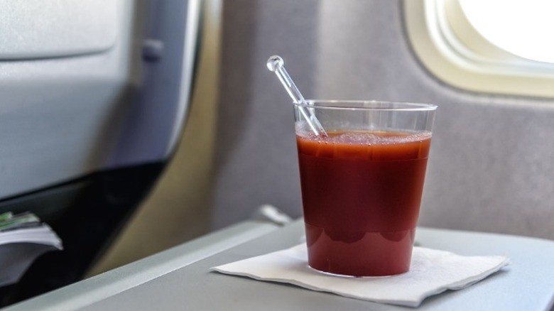 A plastic cup of tomato juice on a fold-out tray on an airplane
