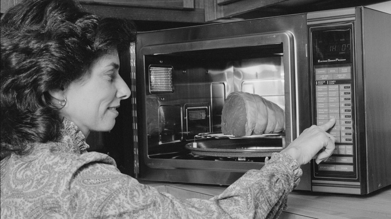 Woman pressing buttons on a microwave containing food in 1980s