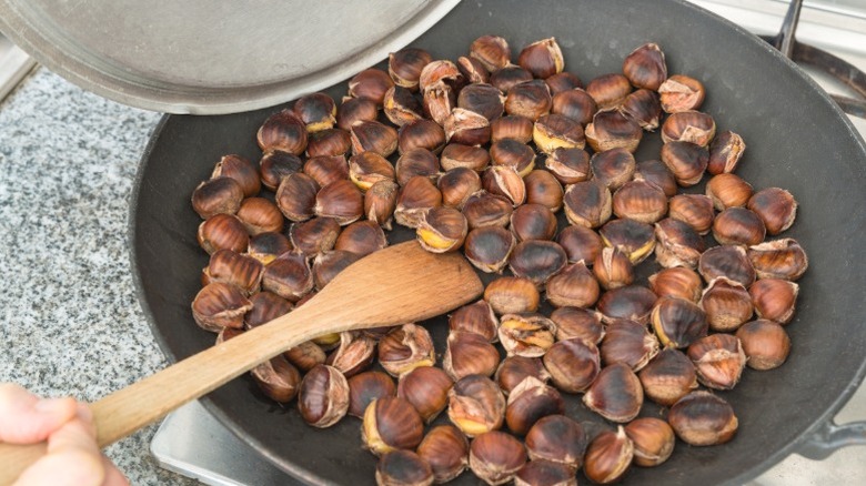 Chestnuts being roasted in a pan with a wooden spoon