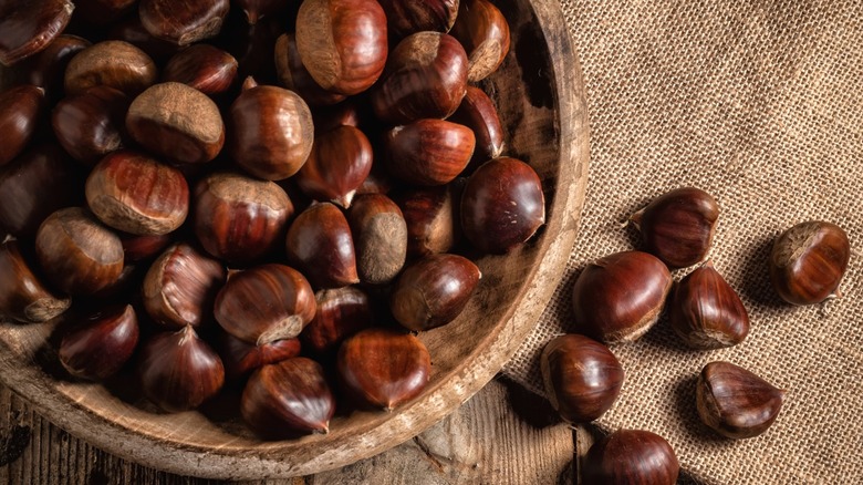 A wooden bowl of chestnuts on a burlap tablecloth