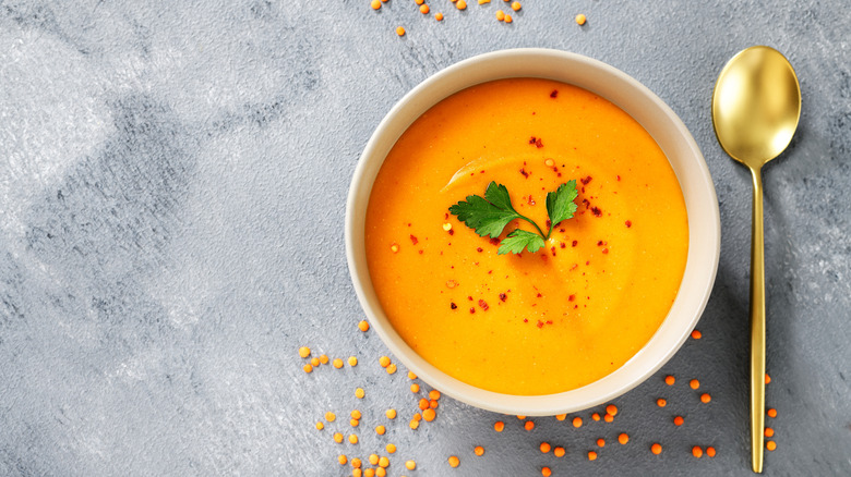 A bowl off creamy orange lentil soup with a herb garnish and a spoon