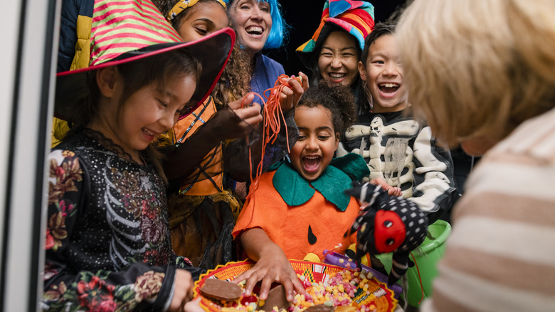 A group of kids on Halloween grabbing candy from a bowl while they trick-or-treat.