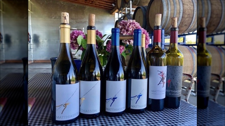 A row of wine bottles on a table with wine barrels in the background