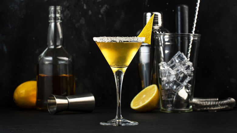 A glass of sidecar cocktail, oranges, and a cocktail shaker and stirrer