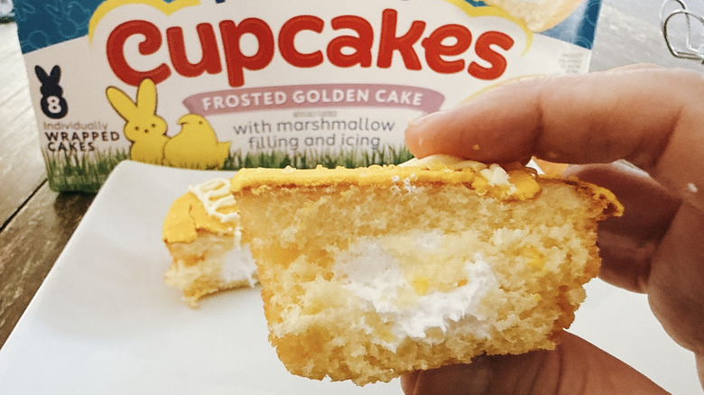 Hostess Peeps cupcake split open to reveal marshmallow filling with the other half of the cupcake on a white plate and the box in background