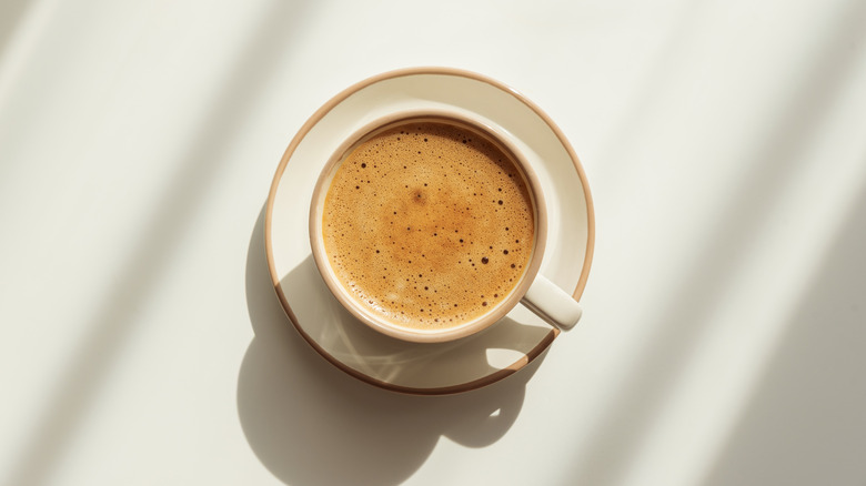 A white coffee cup full of espresso with a rich crema shot from above on a white surface