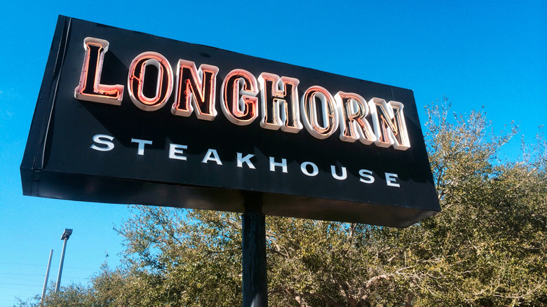 A neon LongHorn Steakhouse sign in front of a blue sky and trees