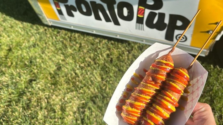 hand holding Pronto Pups in front of Pronto Pup stand