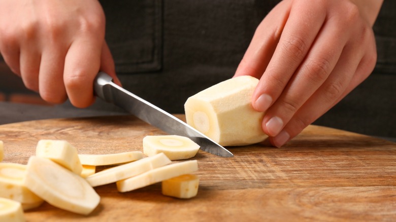 Person cutting parsnip on wood board