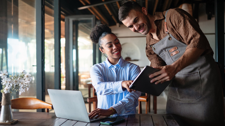 Two restaurant workers talking and holding a laptop and a tablet