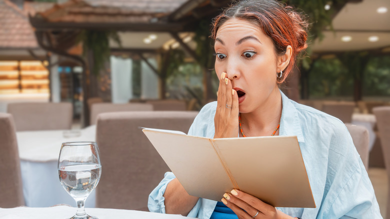 A woman looking at menu with a shocked expression