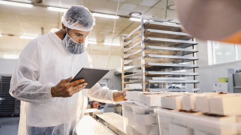 A man with a tablet wearing a hair net and checking food
