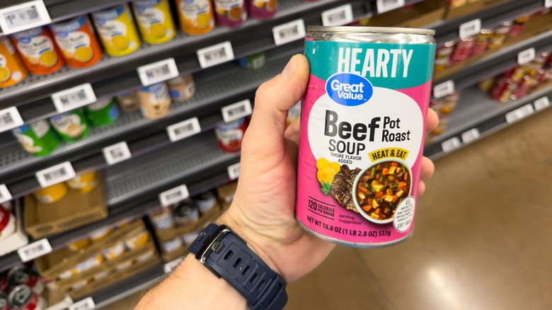 A hand holding a can of Great Value soup in a Walmart store.