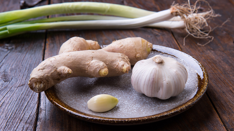 Ginger and garlic on a plate with scallions on a wooden table