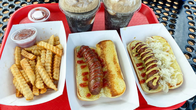 Bratwurst sausages in buns with a variety of condiments and side dishes including fries and rootbeer floats
