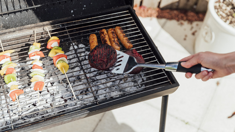 High-angle view of a hand using a spatula to flip a burger on a grill.
