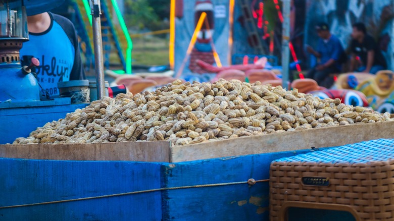 A blue cart selling a large amount of boiled peanuts out of a brown box.