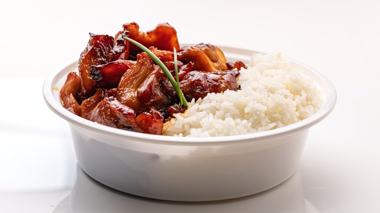 A Chinese takeout container of bourbon chicken and white rice.