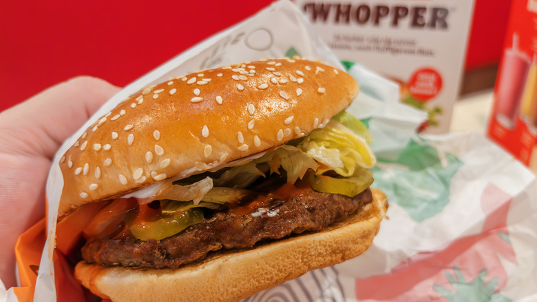 A person holding a Burger King Whopper still partially in its wrapper
