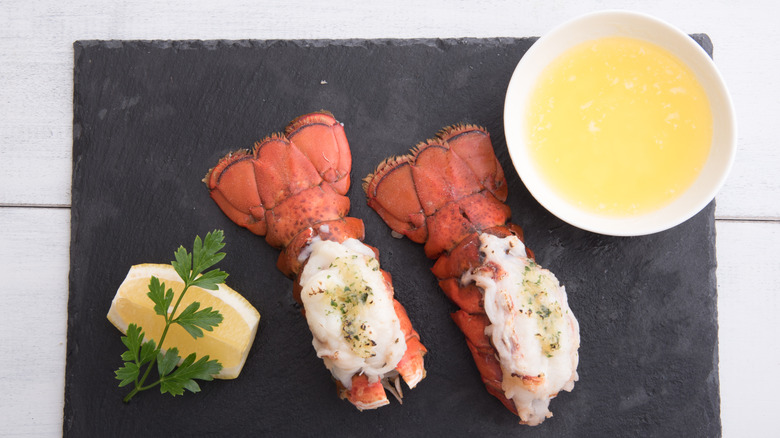 Two cooked lobster tails sitting on a plate with butter and lemon