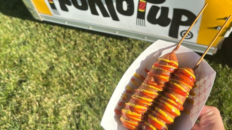 hand holding Pronto Pups in front of Pronto Pup stand