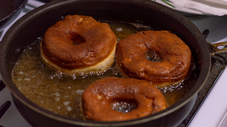 Three donuts frying in a pan.