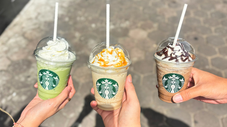 Three hands holding assorted Starbucks Frappuccinos