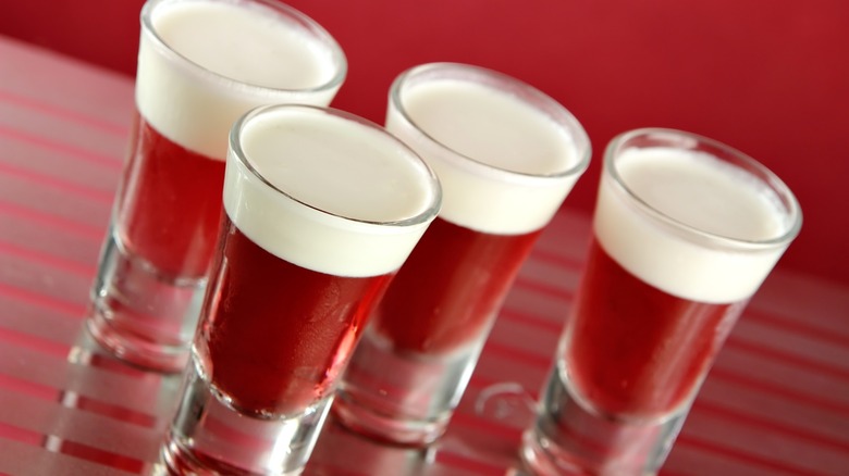 Red Jell-O shots with cream on a striped red surface.