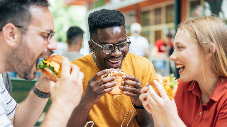 Three people smiling and enjoying hamburgers