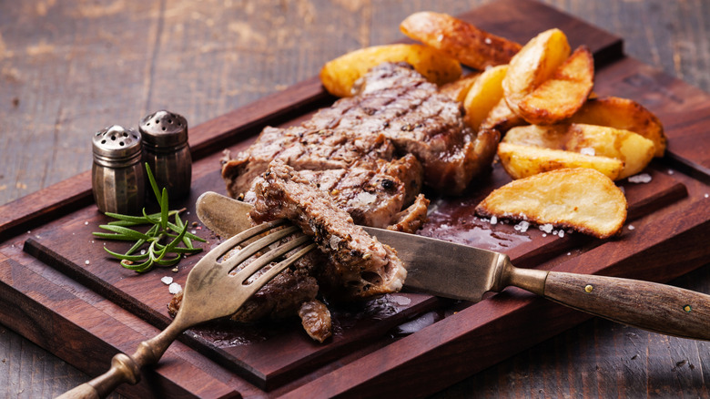 Sliced up well-done steak with potato wedges