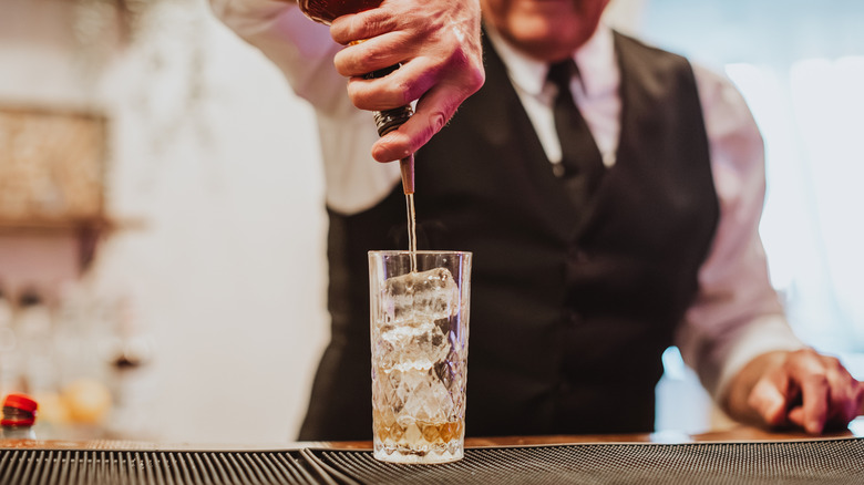 Bartender pouring liquor into glass with ice