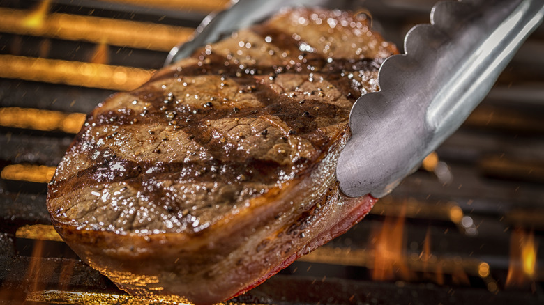 Metal tongs picking up grilled steak off of grill