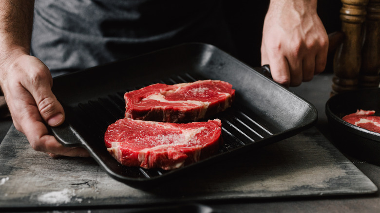 A man holding a grill plate with two raw steaks on it ready to be cooked.