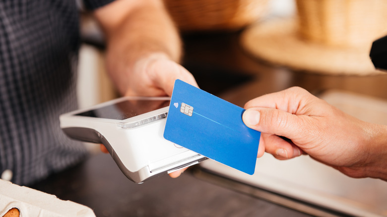 A hand extends a credit card to a payment device held by another hand
